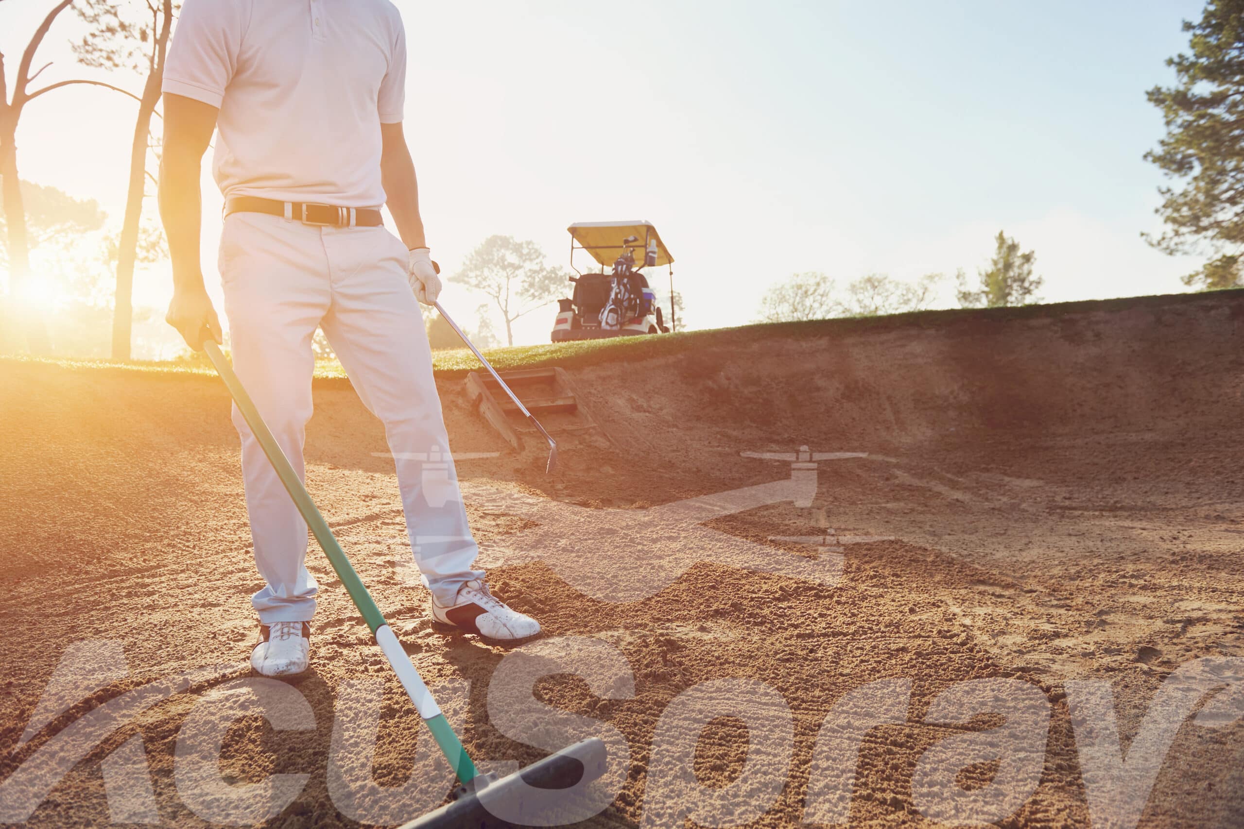 Golf course maintenance worker diligently raking a sand bunker at sunrise.