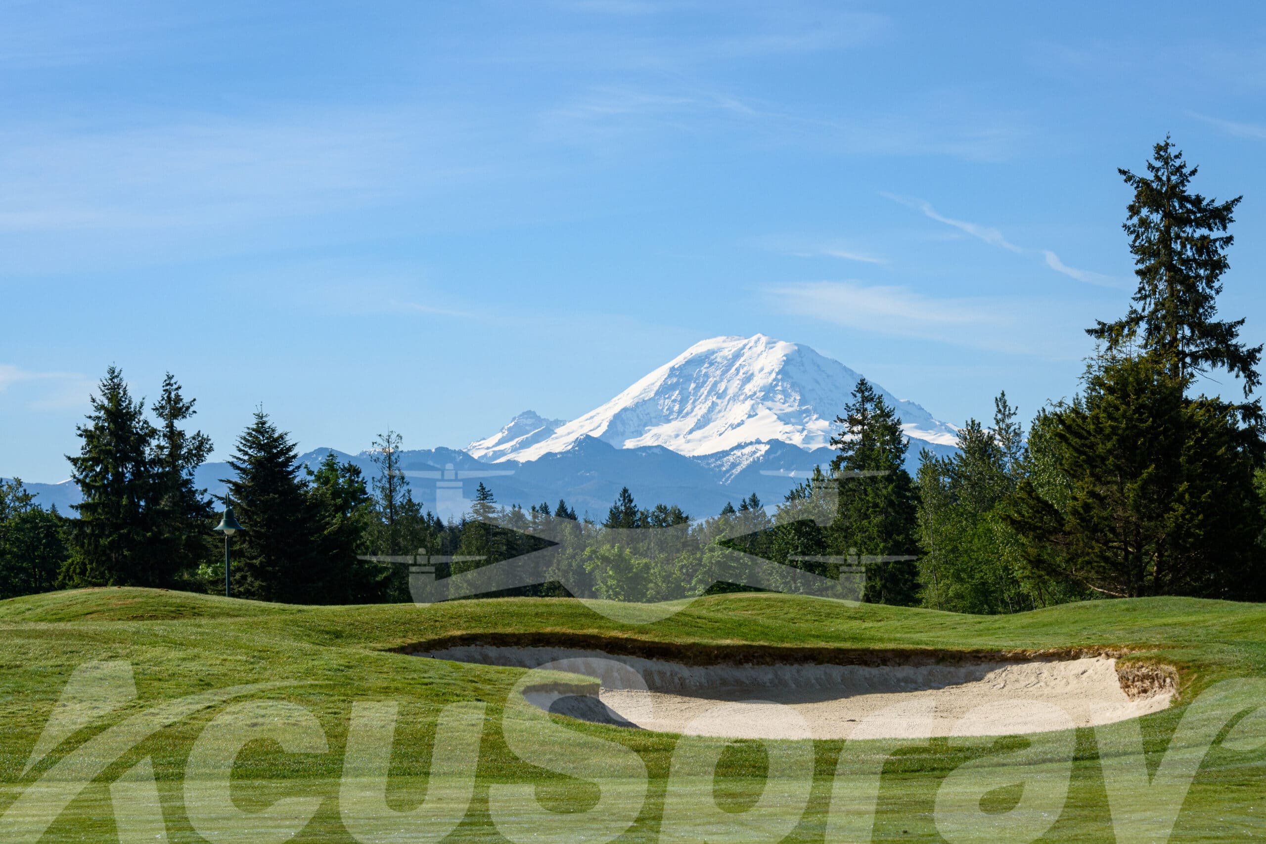 Green fairway with bright sand trap in foreground, majestic Mt Rainier standing tall in the background on a clear day.