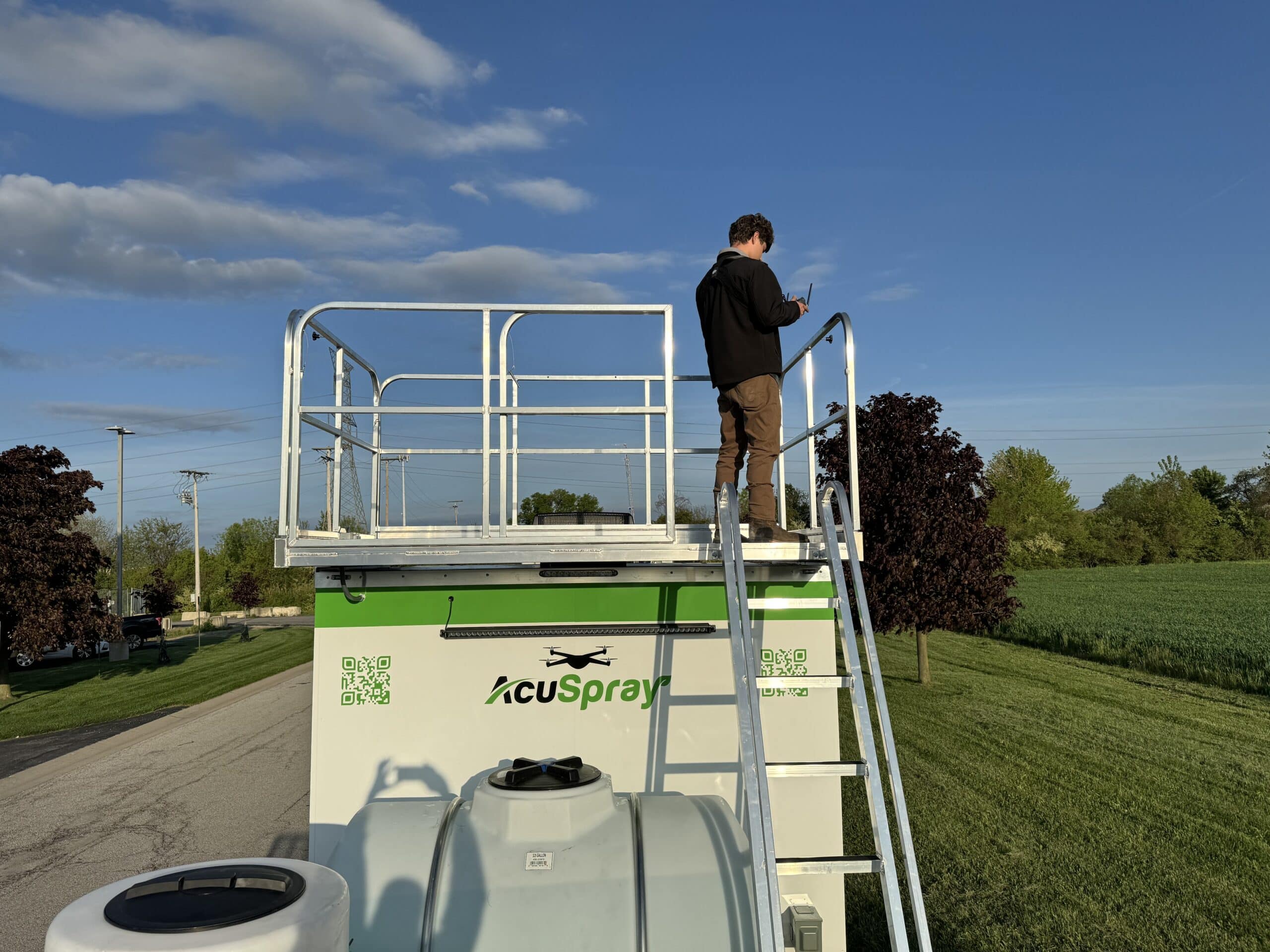 A technician stands on top of an AcuSpray trailer, setting up drone equipment for advanced golf course management, focusing on precise turf care and efficient resource use.